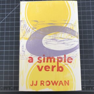 A copy of a simple verb by JJ Rowan on a black gridded cutting mat. The hand-printed linocut cover design is made up of two large yellow semicircles and a large lavender open oval, overlapping. Red lettering spells out the title and author’s name.