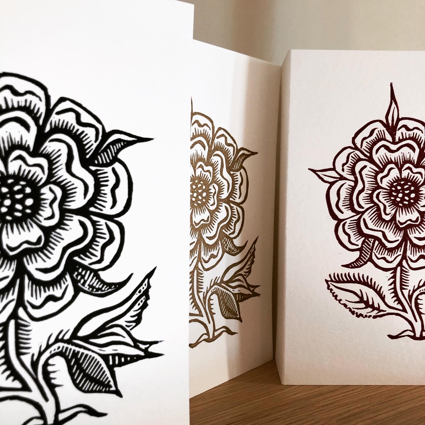 Three hand-printed linocut cards featuring a wild rose in red-violet, midnight blue, and metallic gold.
