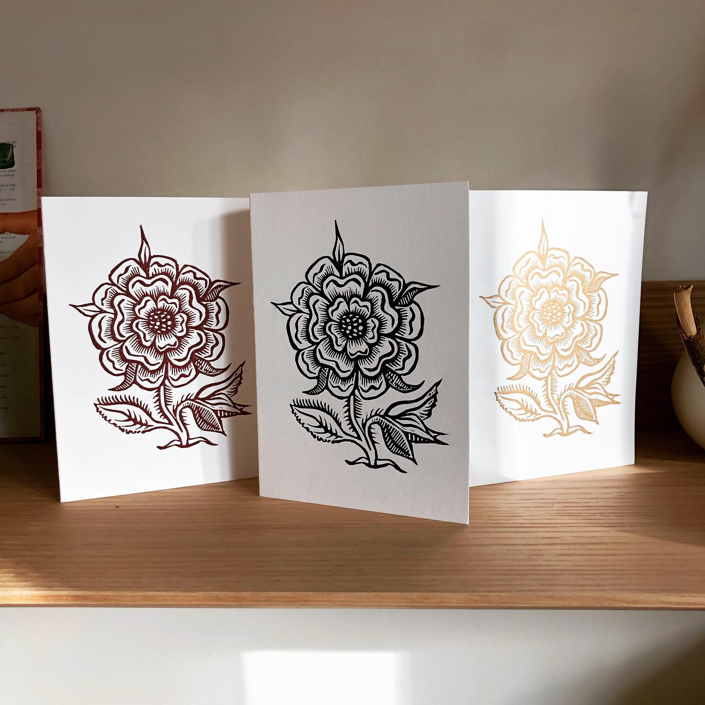 Three hand-printed linocut cards featuring a wild rose in red-violet, midnight blue, and metallic gold.