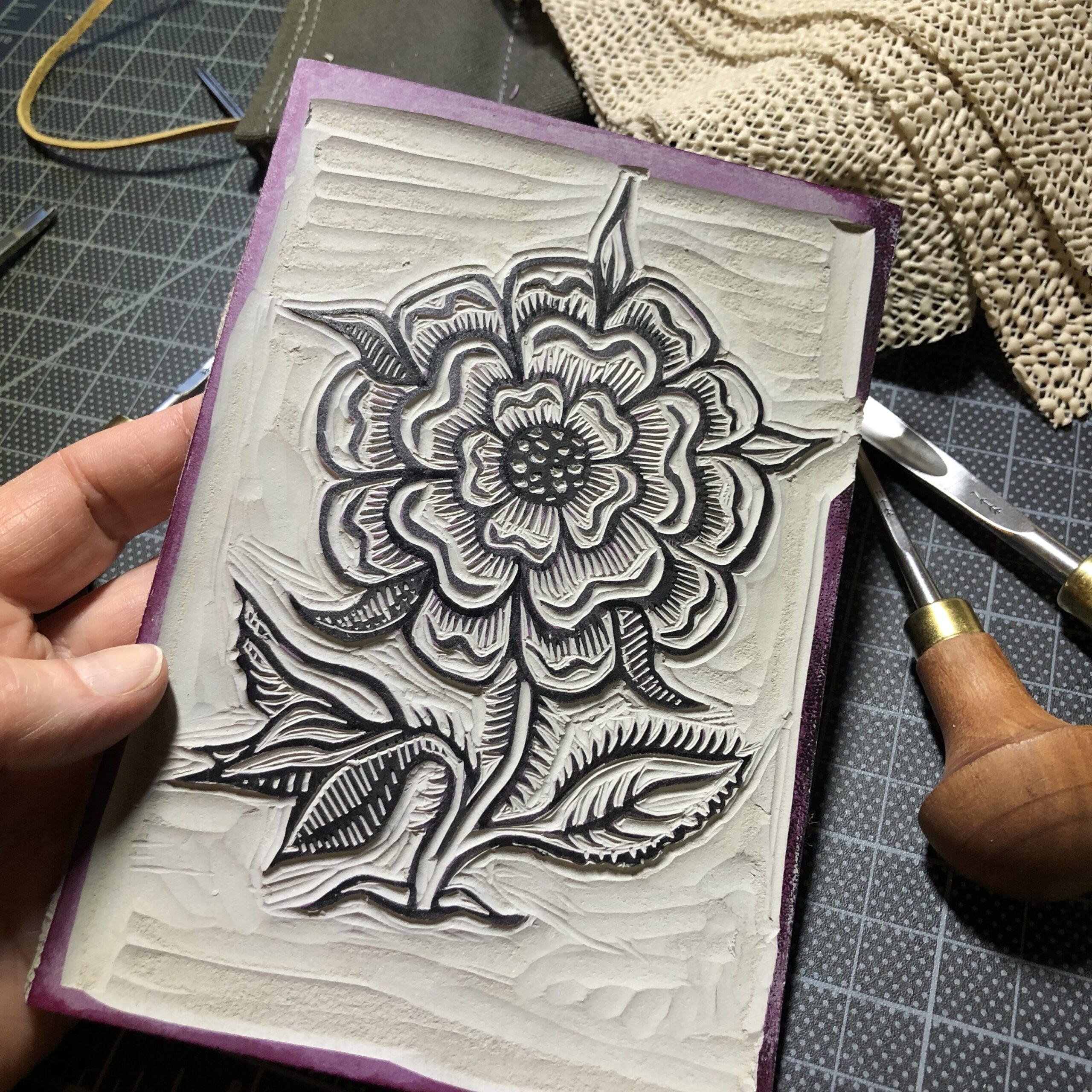 The handcarved linocut block for the wild rose, with cutting tools and nonslip mat to the right.