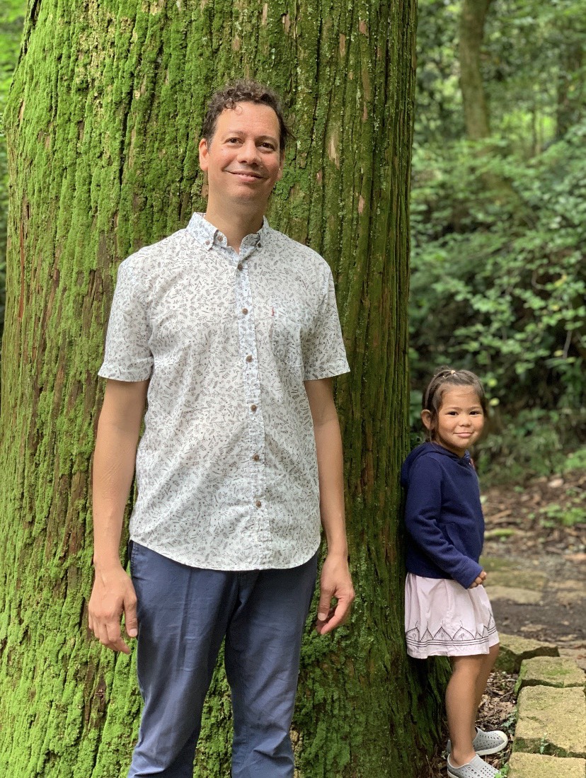 Steven Karl standing in front of a tree with his little daughter.