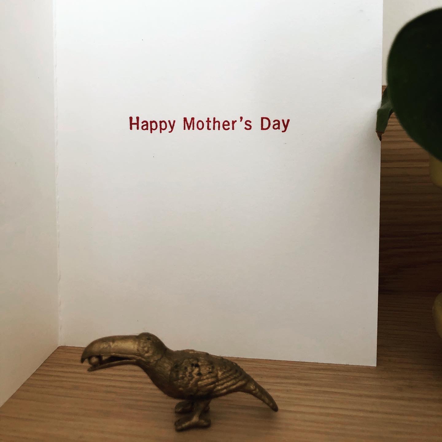 A white card open on a shelf to show the greeting, “Happy Mother’s Day,” in mulberry red ink.